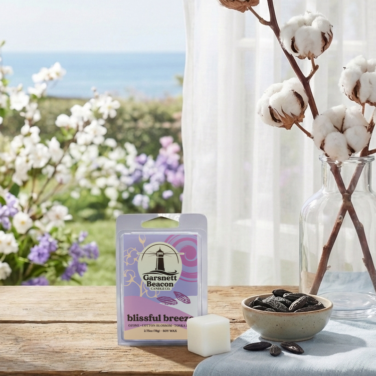 Wax melt packaging on a table with a scenic background of flowers and ocean.