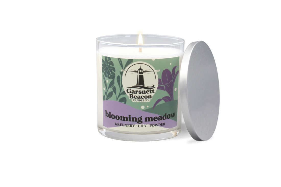 Candle labeled 'Blooming Meadow' with a bouquet of flowers on a windowsill.