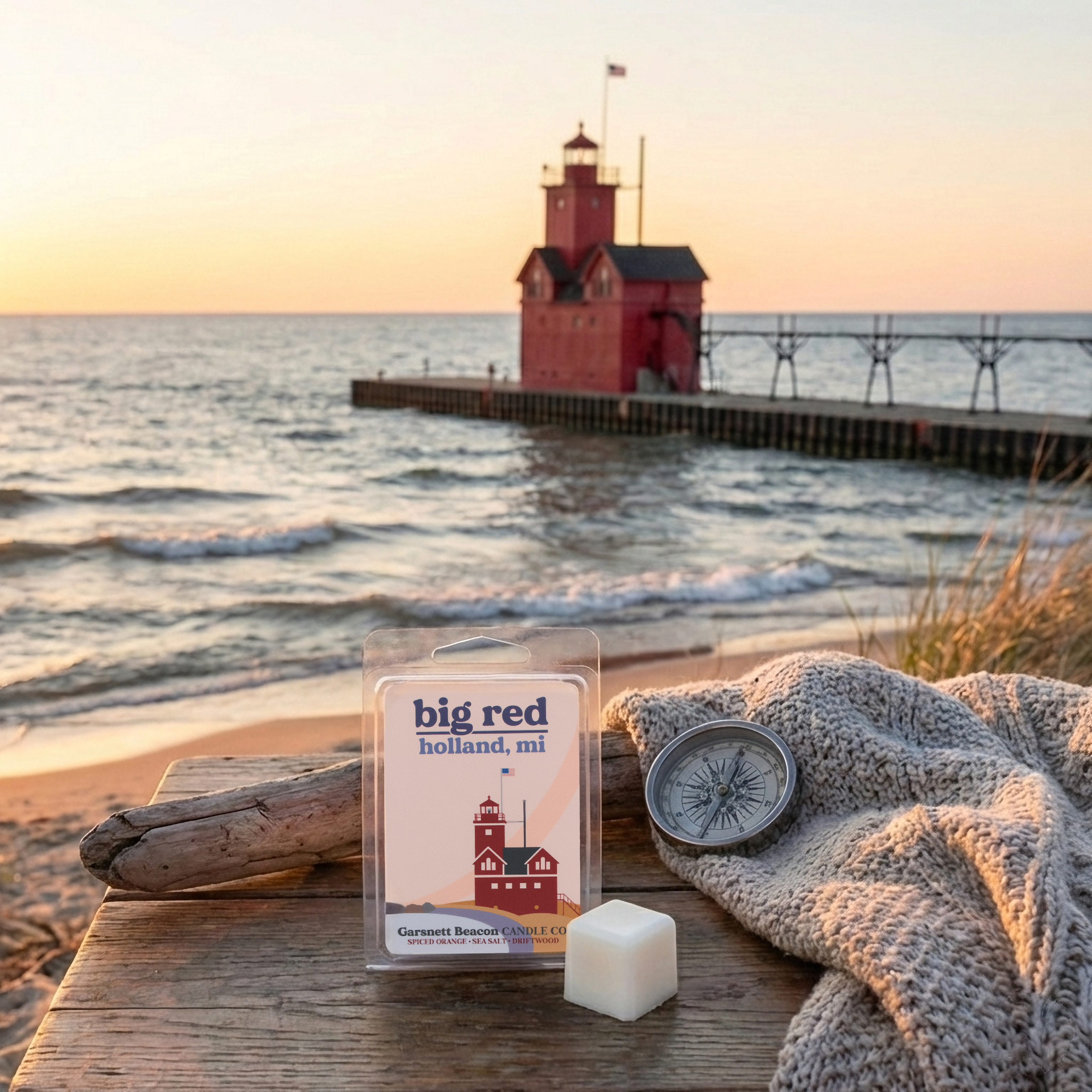Big Red lighthouse wax melt with a compass and blanket on a beach at sunset