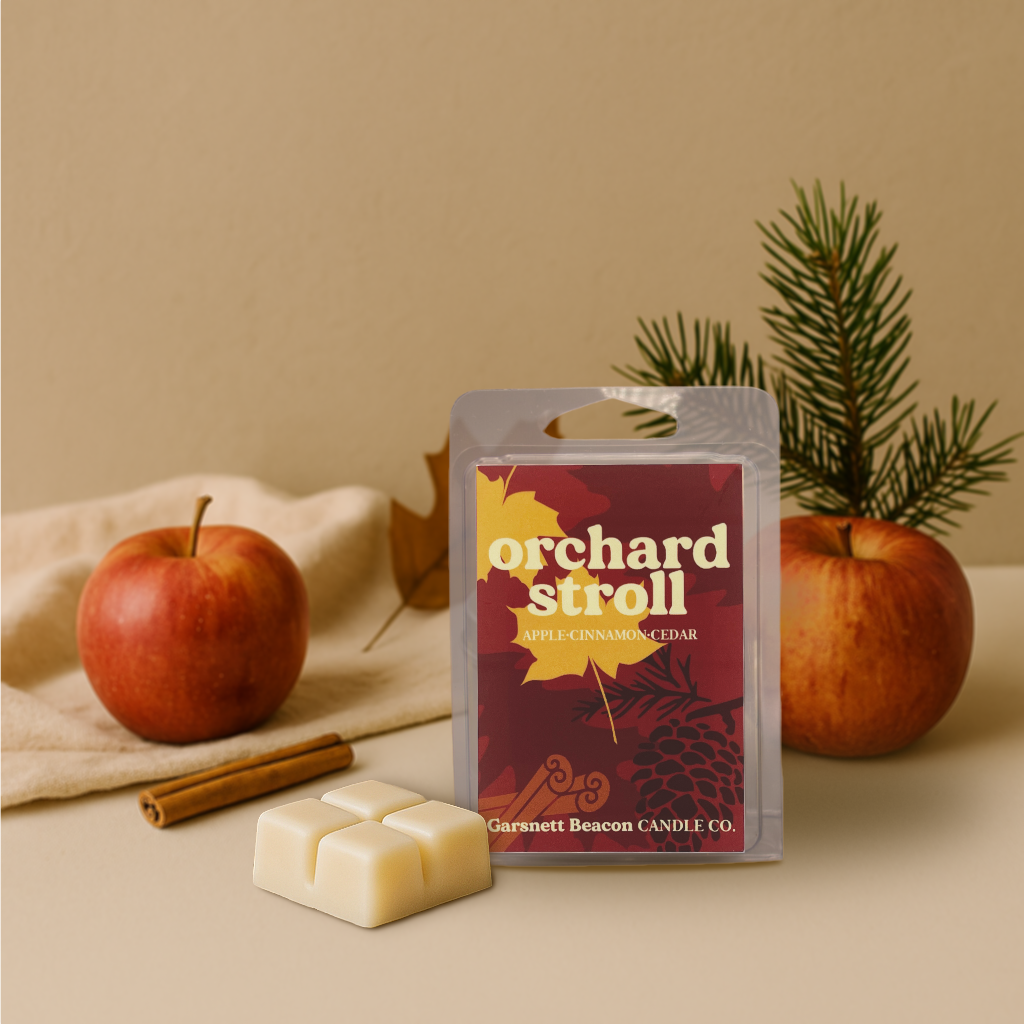 Wax melt packaging with 'Orchard Stroll' label surrounded by apples, cinnamon sticks, and a plant on a beige background