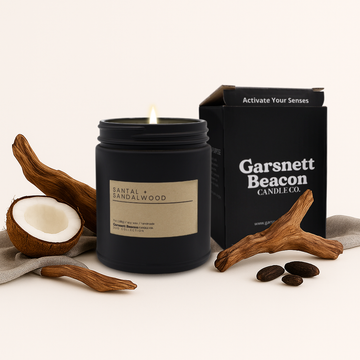 Black candle with 'Garsnett Beacon Candle Co.' packaging, coconut, and wood elements on a light background