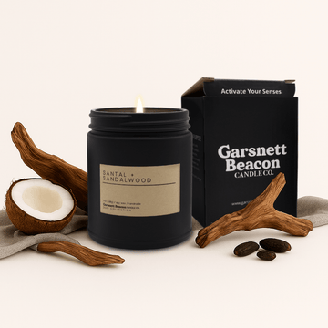 Black candle with 'Garsnett Beacon Candle Co.' packaging, coconut, and wood elements on a light background