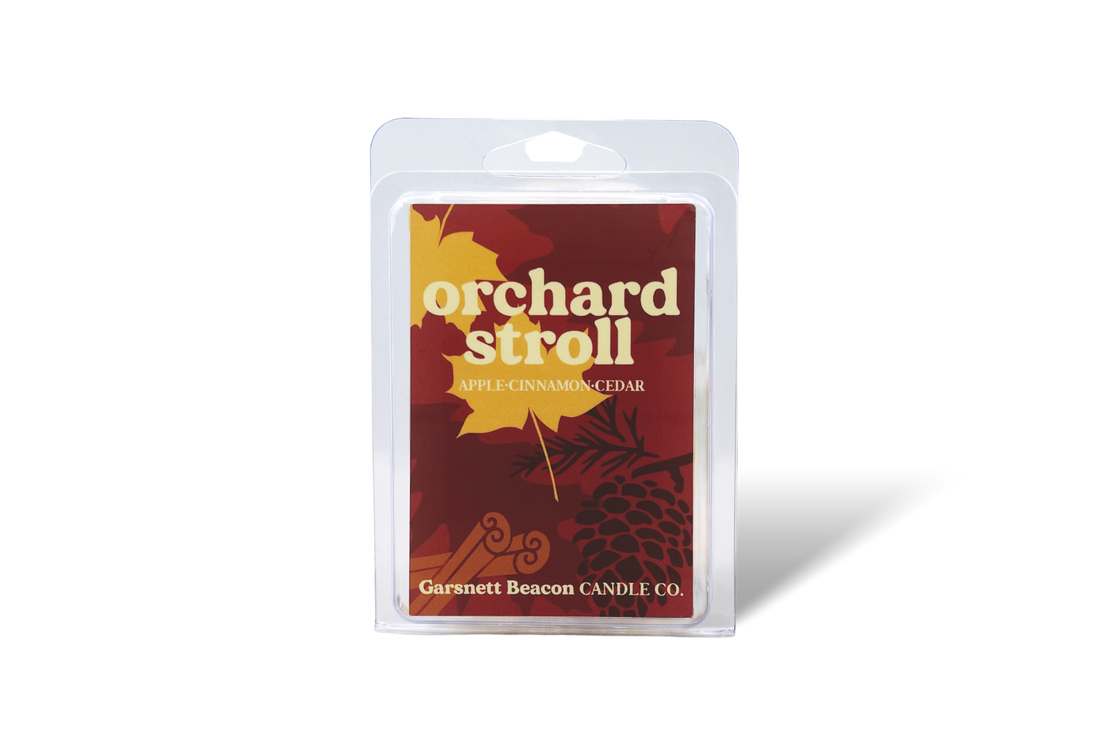 Wax melt packaging with 'Orchard Stroll' label surrounded by apples, cinnamon sticks, and a plant on a beige background