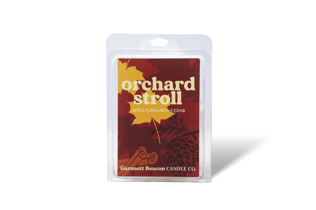 Wax melt packaging with 'Orchard Stroll' label surrounded by apples, cinnamon sticks, and a plant on a beige background